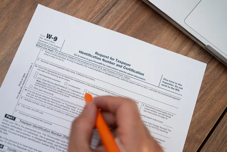Hand completing an IRS Form W-9 with an orange pen